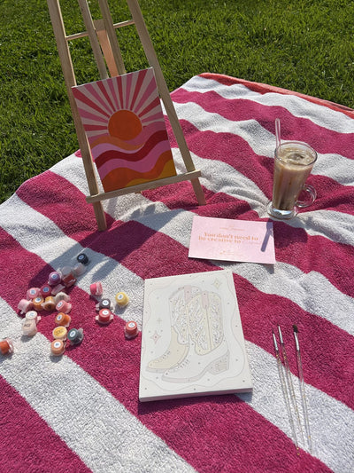 A paint by numbers easel set up on a picnic blanket