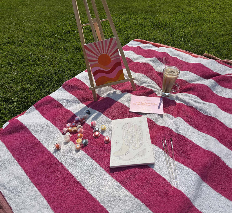 A paint by numbers easel set up on a picnic blanket