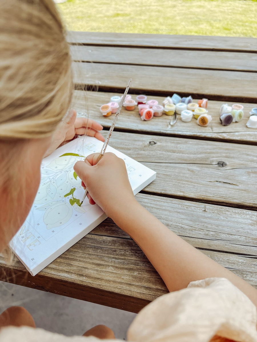 A child painting a canvas at an outdoor bench